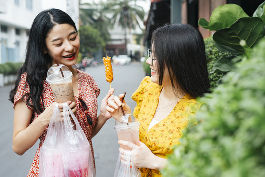 在泰国，两位美丽的亚洲年轻女子喜欢在街上吃美食，走在街上。