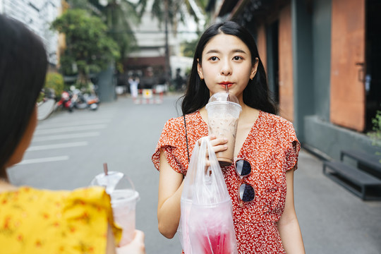 穿着红裙子的亚洲美女和穿着黄裙子的朋友一起吃街边小吃。