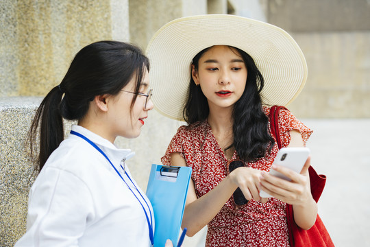 年轻开朗的亚洲旅行家妇女在城市里迷路了。向旅游指南询问信息。在智能手机上显示地图。