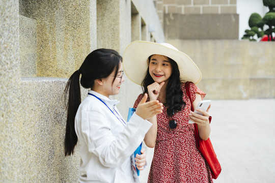 年轻开朗的亚洲旅行家妇女在城市里迷路了。向旅游指南询问信息。在智能手机上显示地图。