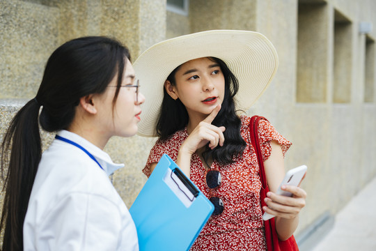 年轻开朗的亚洲旅行家妇女在城市里迷路了。向旅游指南询问信息。在智能手机上显示地图。
