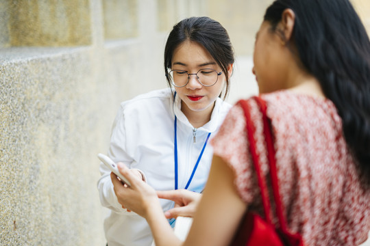 美丽的亚洲导游女士在街上用智能手机给旅行者指路。