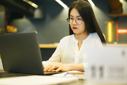 美丽的亚洲女职员戴着眼镜在办公室的笔记本电脑上工作。