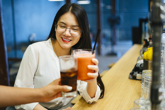 美丽的亚洲女人戴着眼镜坐在酒吧里，和陌生人一起喝彩或祝酒。