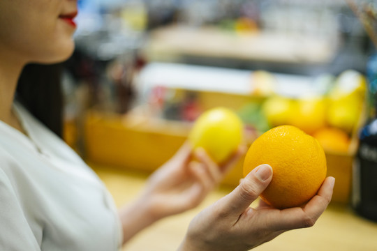 美丽的亚洲女人在超市挑选橘子和柠檬。健康食品选择。维生素C水果。