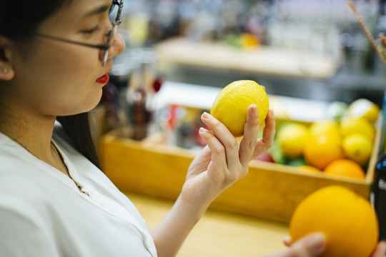 美丽的亚洲女人在超市挑选橘子和柠檬。健康食品选择。维生素C水果。