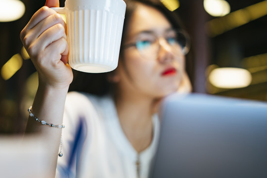 咖啡休息时间——亚洲办公室的女人晚上拿着一杯咖啡在电脑前加班。