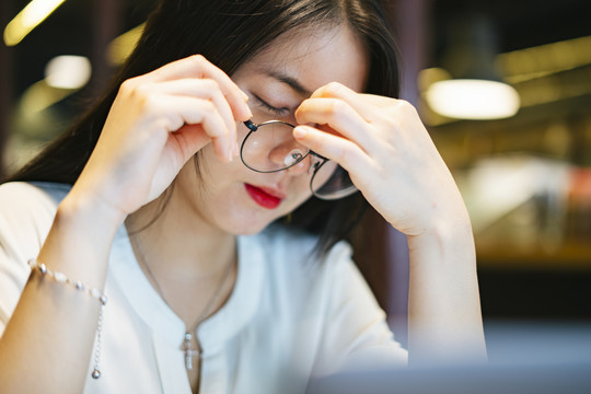 疲惫紧张的亚洲女人戴着眼镜坐在笔记本电脑前。加班加点。疲惫不堪。