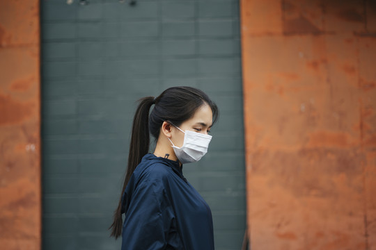 戴着面具的亚洲妇女在烟雾弥漫的城市中行走的侧视图。