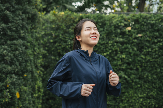 穿着运动服的漂亮女人在公园慢跑，脸上带着微笑。健康活动，跑步锻炼。