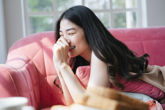 波浪长发女孩趴在家里的粉色沙发上，和男友在电话边谈笑风生。