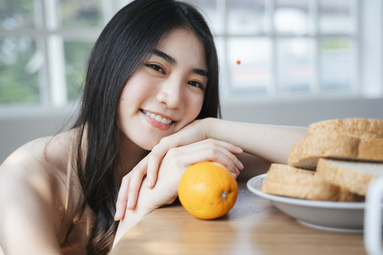卷发女孩坐在餐厅里拿着面包和橘子，把头靠在桌子上。