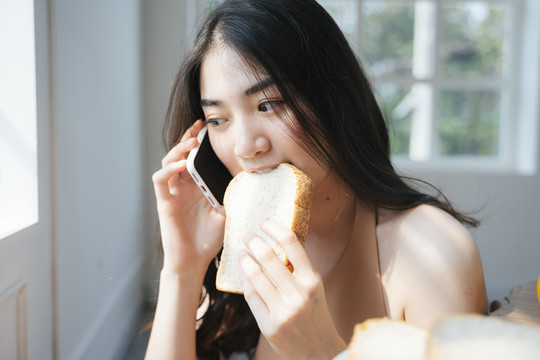 卷曲的长发女孩坐在餐厅的窗边，一边咬着面包一边和男友聊天。