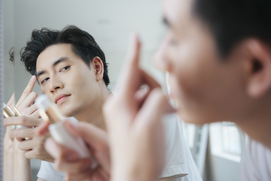 一个穿白色t恤的男人在镜子前把乳液涂在脸上。