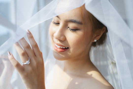 马尾金发女人在婚礼当天的早晨打扮好，站在窗前，用白色面纱遮住自己，摸了摸窗户，露出她的结婚戒指。