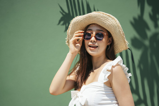 绿色背景下戴帽子和太阳镜的美女肖像。暑假在沙滩上。