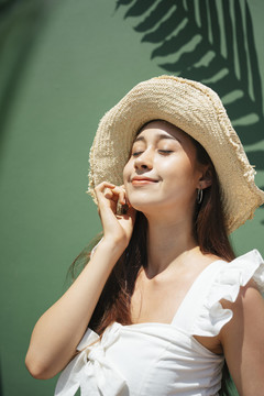 在绿色背景下戴帽子的亚洲美女的特写肖像。在夏天面对阳光。在海滩度过漫长的周末。紫外线防护。