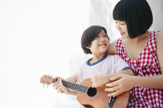 可爱的亚洲妹妹在房间里教她的弟弟如何弹四弦琴。教乐器。