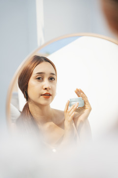 美丽迷人的黑发女人拿着化妆瓶在镜子前化妆。