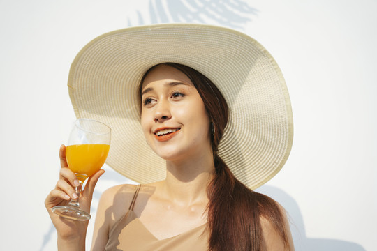 漂亮漂亮的黑发女人戴着大帽子拿着橙汁。夏天喜欢喝果汁。来自农场的新鲜橙汁。