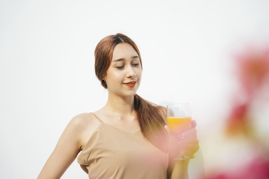 美丽迷人的黑发女人喜欢喝橙汁在玻璃杯隔离在白色背景。