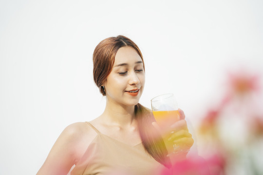 美丽迷人的黑发女人喜欢喝橙汁在玻璃杯隔离在白色背景。