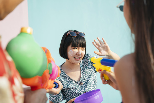 年轻的泰国bob发型漂亮可爱的女孩享受泼水节与人。女人伸手用湿面粉、粉摸人们的脸颊。紫色水碗里的白粘