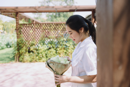 身穿白衬衫的马尾女人站在她家的露台上，举行荷花宴会，面带微笑。