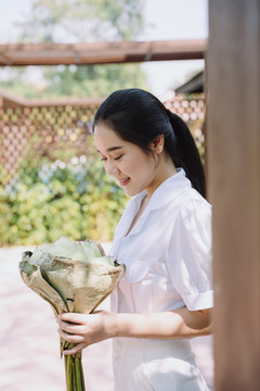 身穿白衬衫的马尾女人站在她家的露台上，举行荷花宴会，面带微笑。