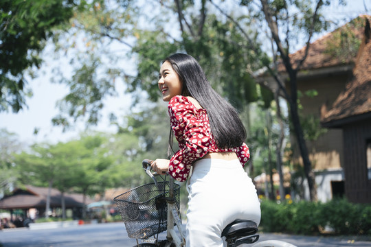 在传统村庄骑自行车的穿红衬衫的黑色长发妇女的背照。