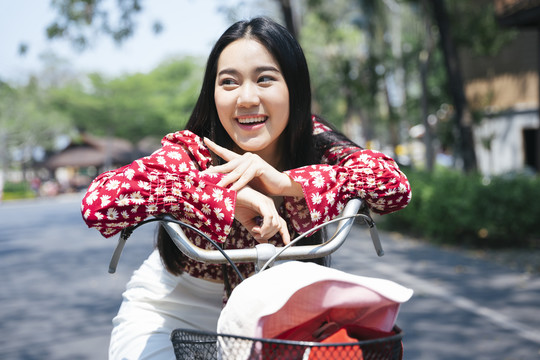 穿红衫的黑色长发女孩在村里停下来骑自行车时，双手托在自行车上。