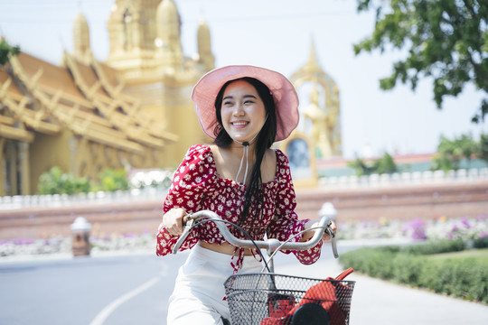 穿着红衬衫、戴着红帽子的黑长发女孩骑着自行车在传统的城镇和寺庙里转来转去。