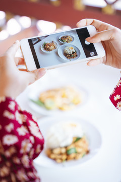 穿着红衬衫的女人用智能手机拍下餐厅桌上食物的照片时，智能手机的图像被剪短了。