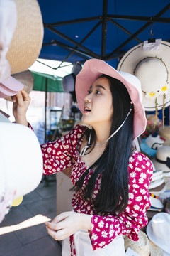 穿红衬衫、戴红帽子的黑色长发女孩喜欢漫步在当地的集市上，看看精彩的商品和产品。