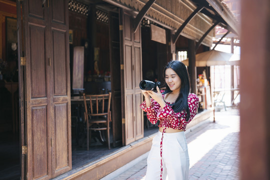 穿红衬衫的黑色长发女孩漫步在传统小镇上，在木屋间合影留念。