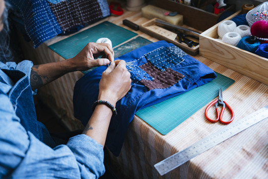 工匠缝制深蓝色织物进行固定时手的裁剪图像。