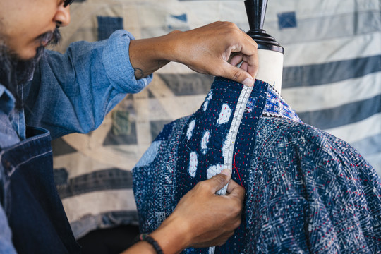 一个穿着蓝色衬衫和围裙的男人在人体模型上测量衣服以使其合身，测量后颈。