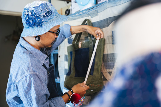 一个穿着蓝色衬衫、帽子和围裙的男人用卷尺量了量袋子，然后拍了张照片在网上卖。