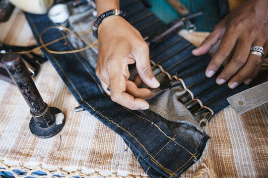 一个穿蓝衬衫的人从工具袋里拿起剪刀修剪皮革。