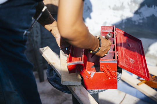 一个男人手里拿着一个红色工具箱，在完成工作后，把工具放在盒子里。