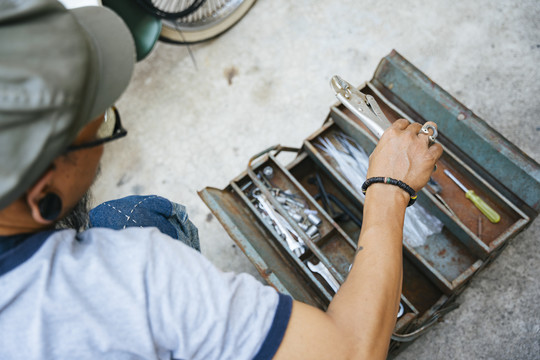 修理摩托车的技工，一个人在家里，用工具箱里的工具。