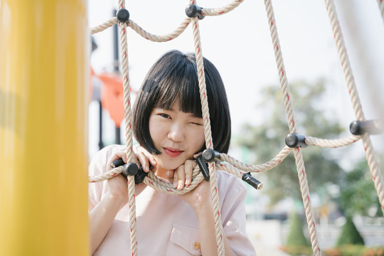 可爱的年轻亚泰女子鲍勃发型玩绳子在操场区户外暑假。