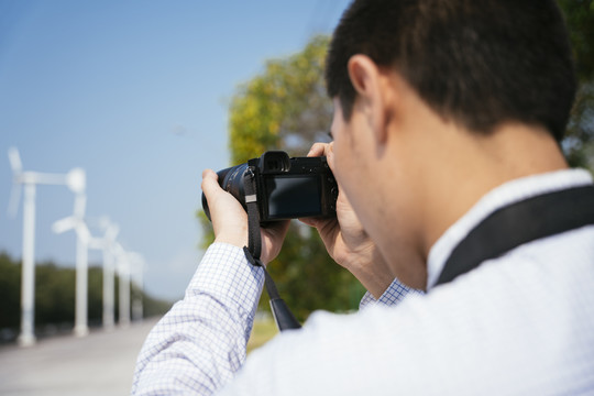光头摄影师用相机拍摄风车的后景。