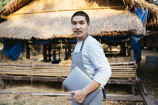 生态旅游——光头当地农民手持笔记本电脑的画像。农民用科技做生意。