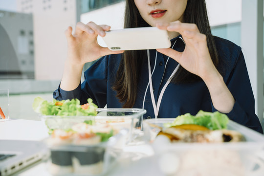 亚洲女人用智能手机拍照。餐桌上的健康食品。先吃饭。