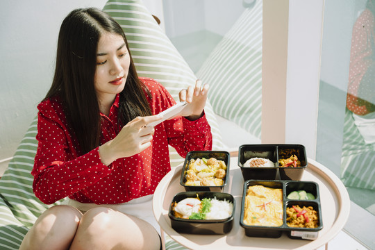 美丽的亚泰黑发红衫女子用智能手机拍摄美食美酒。先吃饭。