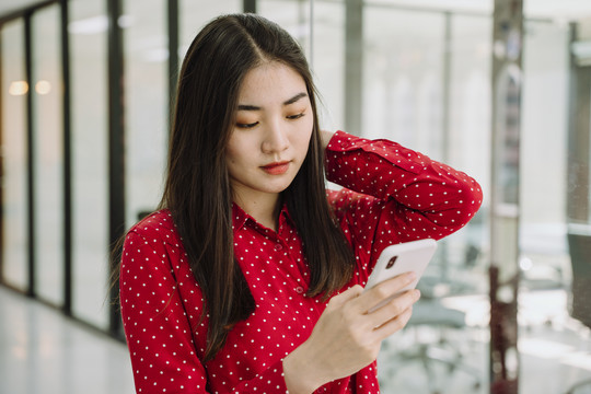 美丽的亚泰长黑发红衫女子用智能手机。