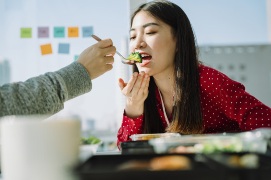 年轻漂亮的亚泰女商人喜欢和朋友在家吃饭。一个男人用蔬菜喂女孩的手。