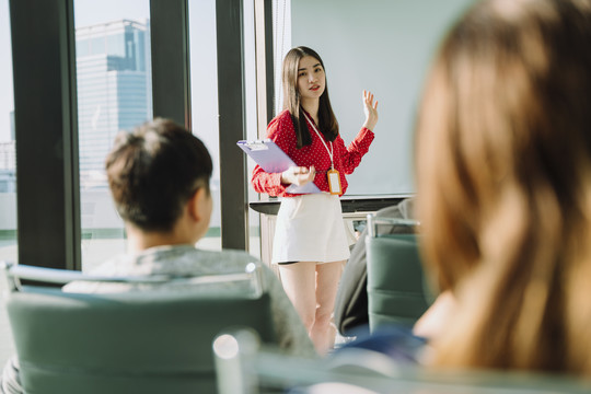 在会议室里，身着红衫的美丽的年轻亚泰女商人在人们面前做报告。人们举手向她提问。