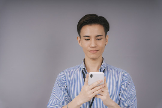 穿着蓝领衬衫的泰国帅哥商人在一台设备上使用智能手机社交网络应用程序。在灰色背景上孤立。
